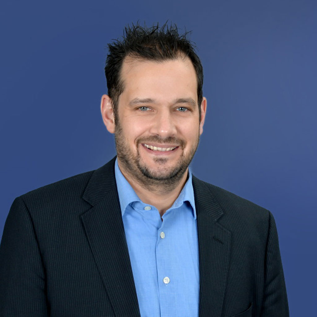 Mann im dunklen Anzug und blauem Hemd lächelnd, ideal für Finanzberatung oder Vermögensplanung.