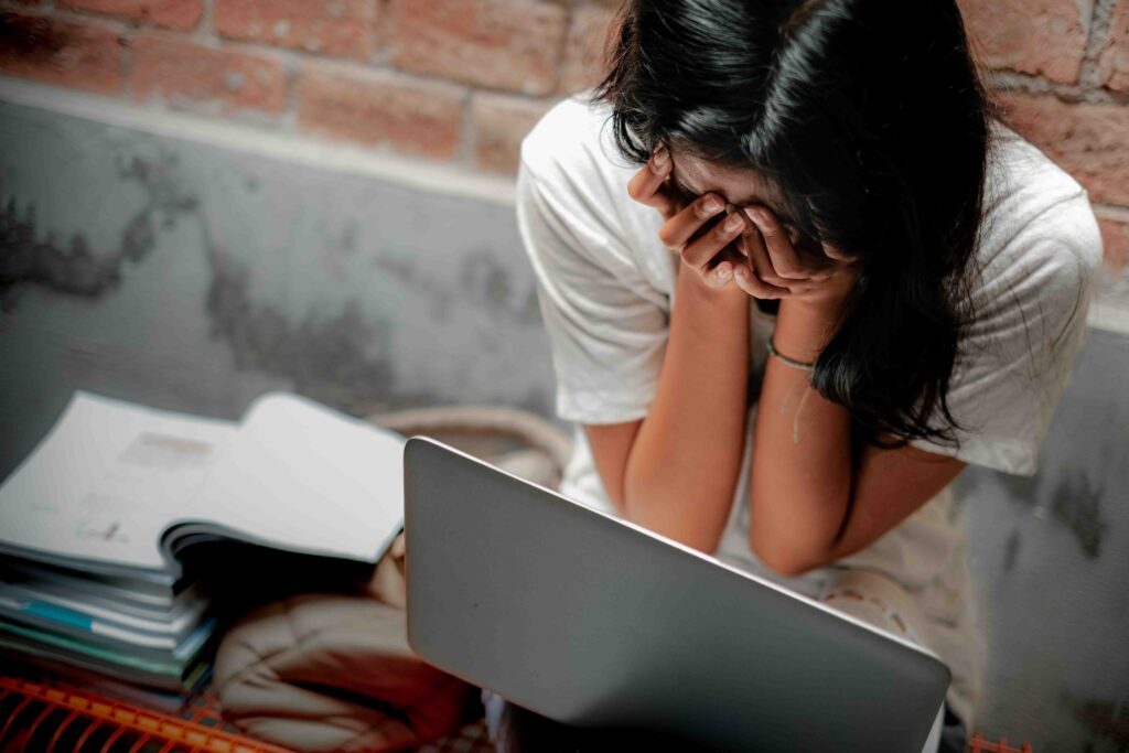 verzweifelte Frau die vor ihrem Laptop sitzt und die Hände vor das Gesciht hält